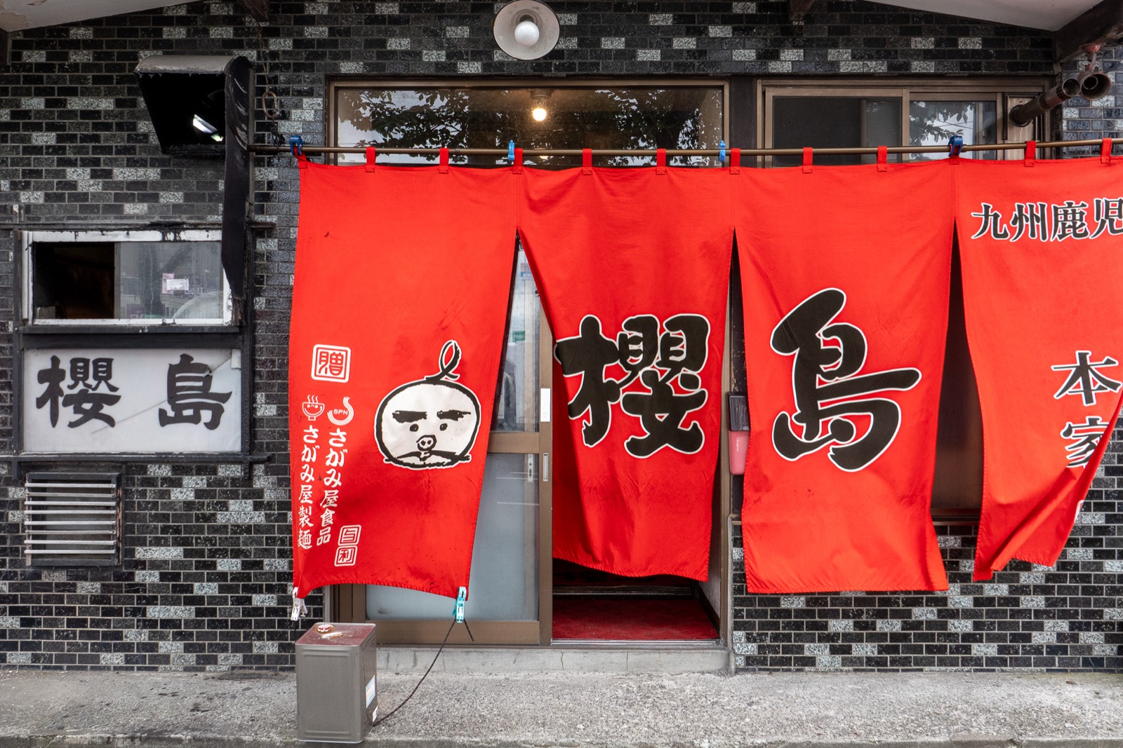 「櫻島」と書かれた赤いのれんのラーメン屋の店先